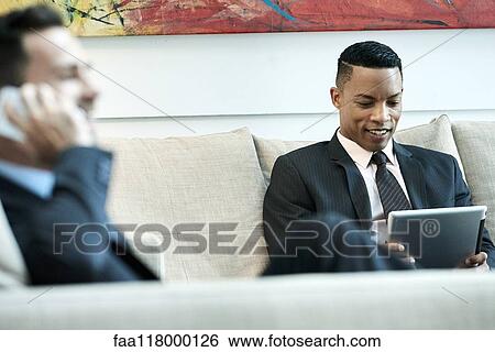Stock Photograph - Businessman using digital tablet in hotel lobby. Fotosearch