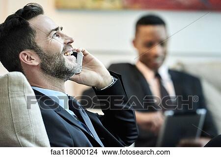 Picture - Businessman using smart phone in hotel lobby. Fotosearch