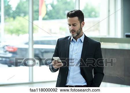 Businessman using smart phone in hotel lobby View Large Photo Image Stock Image - Businessman using smart phone in hotel lobby. Fotosearch