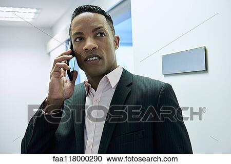 Stock Image - Businessman using smart phone in hotel lobby. Fotosearch