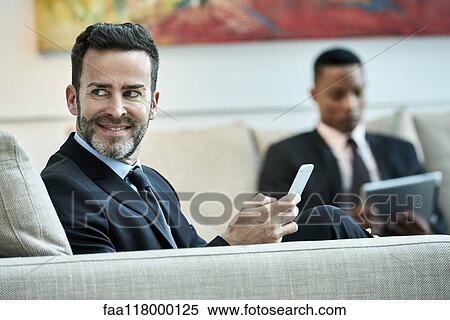 Businessman using smart phone in hotel lobby View Large Photo Image Stock Photography - Businessman using smart phone in hotel lobby. Fotosearch