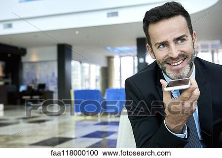 Stock Image - Businessman using smart phone while sitting on sofa. Fotosearch