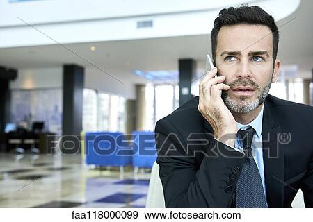 Businessman using smart phone while sitting on sofa View Large Photo Image Stock Photo - Businessman using smart phone while sitting on sofa. Fotosearch