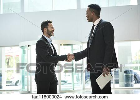 Picture - Businessmen shaking hands in hotel lobby. Fotosearch