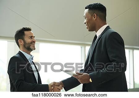 Businessmen shaking hands in office lobby View Large Photo Image Stock Photograph - Businessmen shaking hands in office lobby. Fotosearch