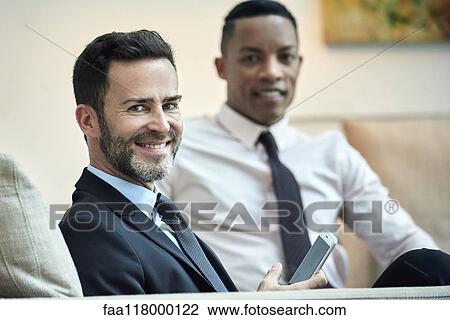 Stock Image - Businessmen sitting in hotel lobby. Fotosearch