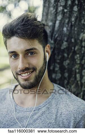 Stock Image - Close-up of smiling young man listening to music. Fotosearch