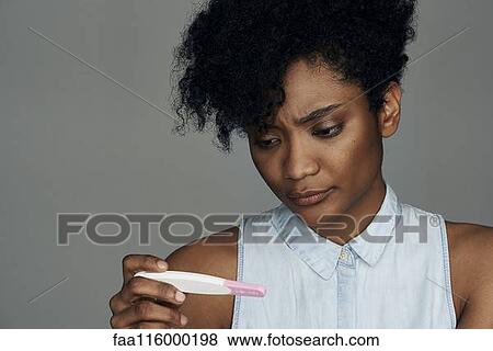 Stock Photo - Close-up of young woman looking at pregnancy test strip. Fotosearch