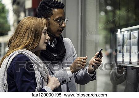Stock Photography - Couple using smartphone at window display. Fotosearch