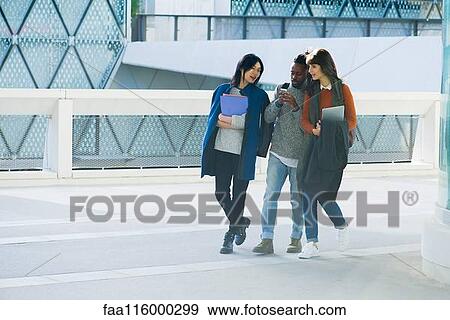 Friends walking together and using smartphone View Large Photo Image Stock Photo - Friends walking together and using smartphone. Fotosearch