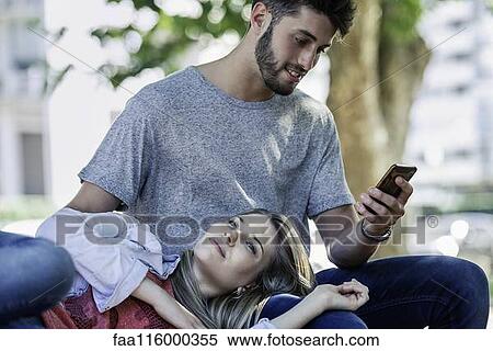 Man using a smartphone while woman relaxing on his lap View Large Photo Image Stock Photography - Man using a smartphone while woman relaxing on his lap. Fotosearch
