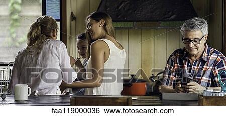 Stock Photograph - Mature man with his family using smart phone in kitchen. Fotosearch