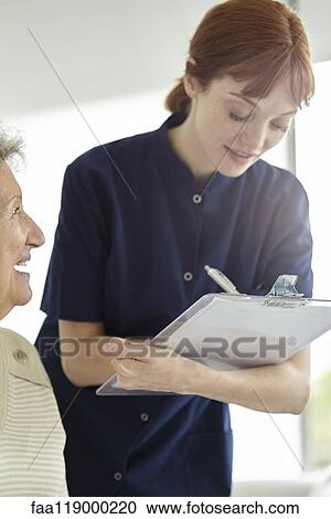 Stock Image - Nurse writing medical history of patient. Fotosearch