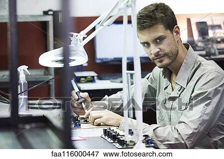 Stock Photo - Portrait of engineer soldering circuit board in office. Fotosearch