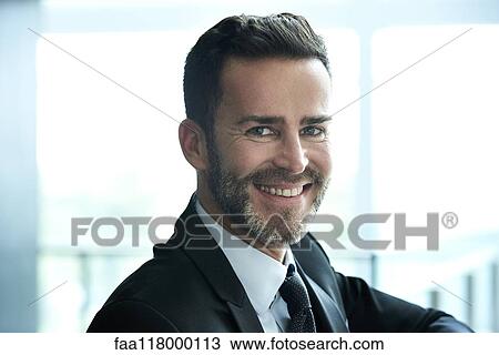 Stock Image - Portrait of smiling businessman standing in hotel lobby. Fotosearch