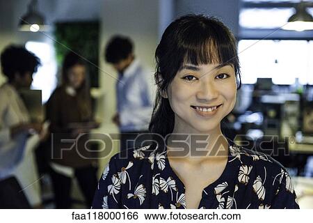 Smiling businesswoman standing in office View Large Photo Image Stock Photograph - Smiling businesswoman standing in office. Fotosearch