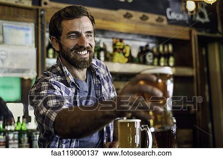 Smiling man serving beer View Large Photo Image Stock Photo - Smiling man serving beer. Fotosearch