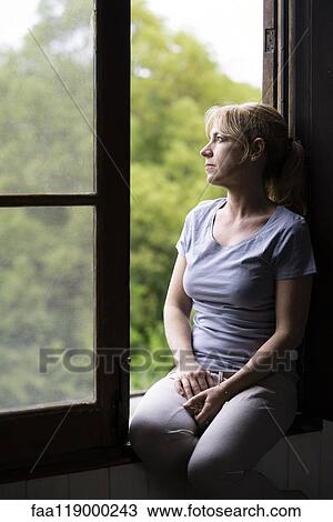 Thoughtful woman sitting on window View Large Photo Image Stock Image - Thoughtful woman sitting on window. Fotosearch