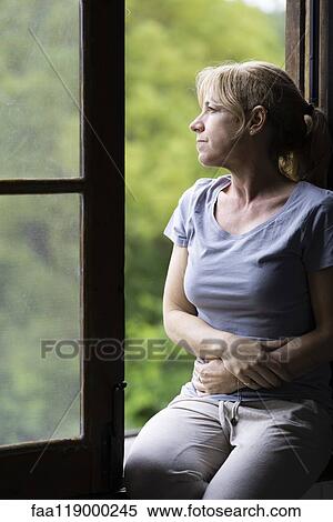 Stock Photography - Thoughtful woman sitting on window. Fotosearch