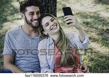 Young couple listening to music and taking selfie with a smartphone View Large Photo Image Stock Photograph - Young couple listening to music and taking selfie with a smartphone. Fotosearch