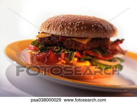 Stock Photo - Cheeseburger with tomatoes, lettuce, and onions on sesame seed bun, on plate, close-up. Fotosearch