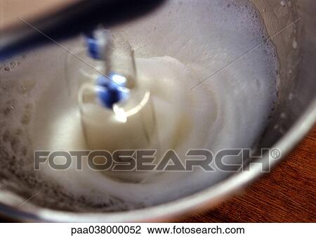 Stock Image - Electric mixer beating egg whites in bowl, close-up. Fotosearch