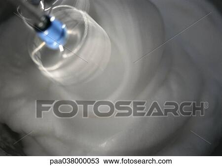 Stock Image - Electric mixer beating egg whites in bowl, close-up. Fotosearch