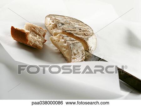 Stock Photograph - Knife, cheese and chunk of bread on paper, close-up. Fotosearch