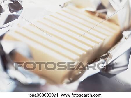 Stock Image - Piece of white chocolate on foil, close-up. Fotosearch