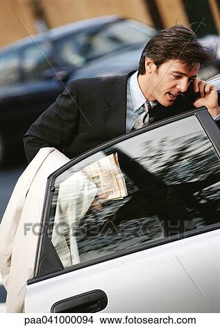 Businessman behind opened car door, using cell phone View Large Photo Image Picture - Businessman behind opened car door, using cell phone. Fotosearch