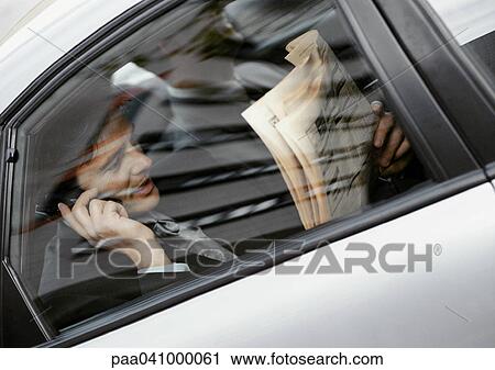 Businessman sitting in back of car, holding newspaper and cell phone, viewed through window View Large Photo Image Stock Image - Businessman sitting in back of car, holding newspaper and cell phone, viewed through window. Fotosearch