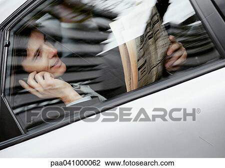 Businessman sitting in back of car, holding newspaper and cell phone, viewed through window View Large Photo Image Stock Image - Businessman sitting in back of car, holding newspaper and cell phone, viewed through window. Fotosearch