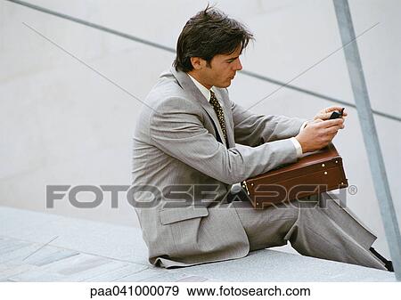 Businessman sitting on stairs, looking at cell phone View Large Photo Image Stock Photo - Businessman sitting on stairs, looking at cell phone. Fotosearch