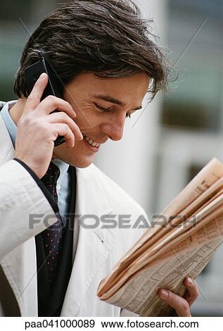 Businessman using cell phone while looking at newspaper View Large Photo Image Stock Photo - Businessman using cell phone while looking at newspaper. Fotosearch