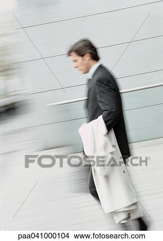 Picture - Businessman walking, holding overcoat, blurred. Fotosearch