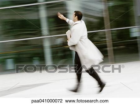 Stock Image - Businessman walking in street, hand raised, blurred. Fotosearch
