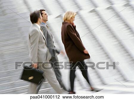 Stock Image - Three business people walking, blurred. Fotosearch