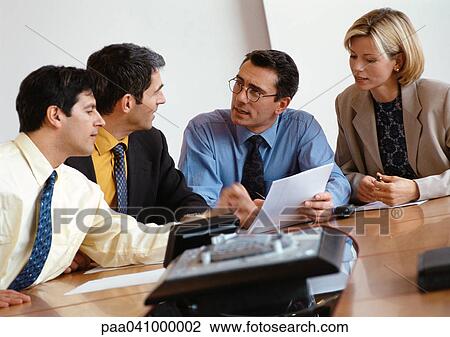 Stock Image - Three businessmen and a businesswoman examining document. Fotosearch