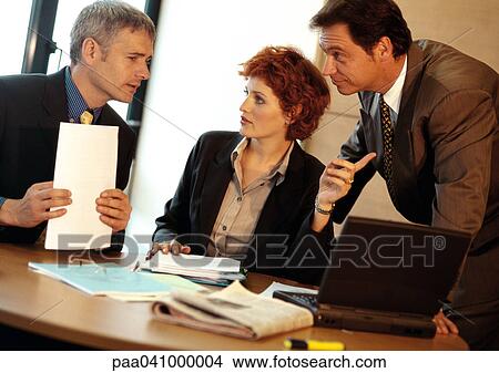 Picture - Two businessmen and a businesswoman around table. Fotosearch