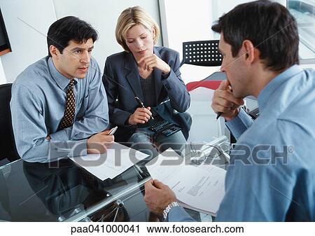 Two businessmen and a businesswoman sitting at desk View Large Photo Image Stock Image - Two businessmen and a businesswoman sitting at desk. Fotosearch
