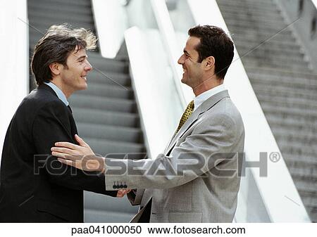 Two businessmen shaking hands in front of stairs View Large Photo Image Stock Image - Two businessmen shaking hands in front of stairs. Fotosearch