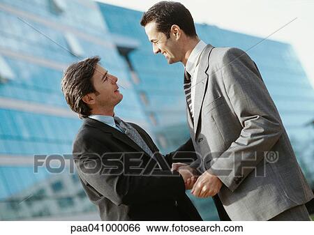 Two businessmen shaking hands, buildings in background View Large Photo Image Stock Photograph - Two businessmen shaking hands, buildings in background. Fotosearch