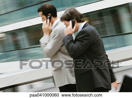Two businessmen using cell phones outside, side view View Large Photo Image Stock Image - Two businessmen using cell phones outside, side view. Fotosearch