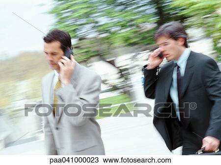 Two businessmen walking outside, holding cell phones, blurred View Large Photo Image Stock Image - Two businessmen walking outside, holding cell phones, blurred. Fotosearch