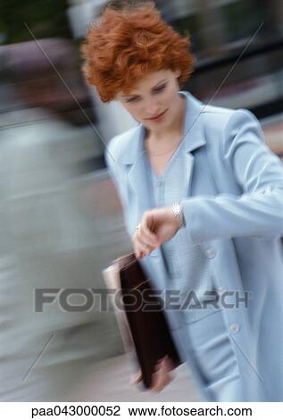 Stock Image - Businesswoman looking at watch, blurred. Fotosearch