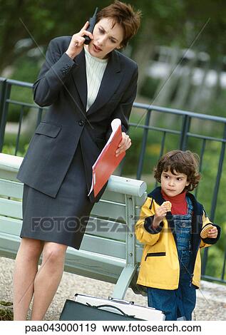 Businesswoman on cell phone next to child eating, outside View Large Photo Image Stock Photo - Businesswoman on cell phone next to child eating, outside. Fotosearch