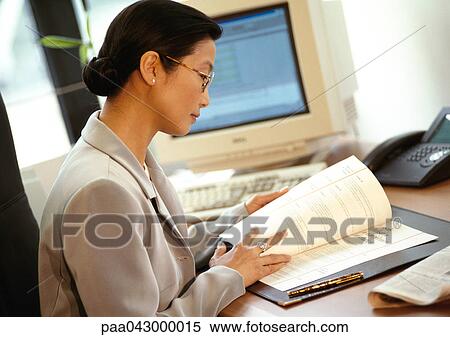 Businesswoman sitting at desk, reading document, side view View Large Photo Image Stock Photography - Businesswoman sitting at desk, reading document, side view. Fotosearch