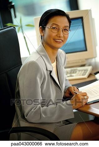 Businesswoman sitting at desk, smiling at camera View Large Photo Image Stock Photograph - Businesswoman sitting at desk, smiling at camera. Fotosearch