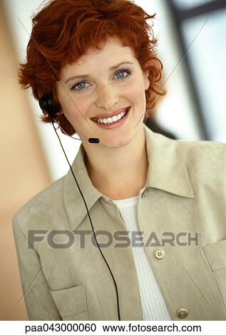 Stock Image - Businesswoman wearing headset, smiling at camera, portrait. Fotosearch