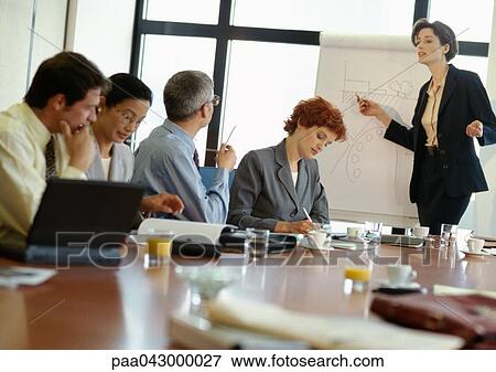 Stock Photo - Group of business people in conference room, businesswoman pointing at presentation board. Fotosearch